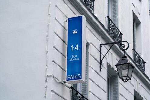 Vertical banner sign mockup on building exterior wall for designers to showcase advertising graphics, with clear sky and wrought-iron lamp.